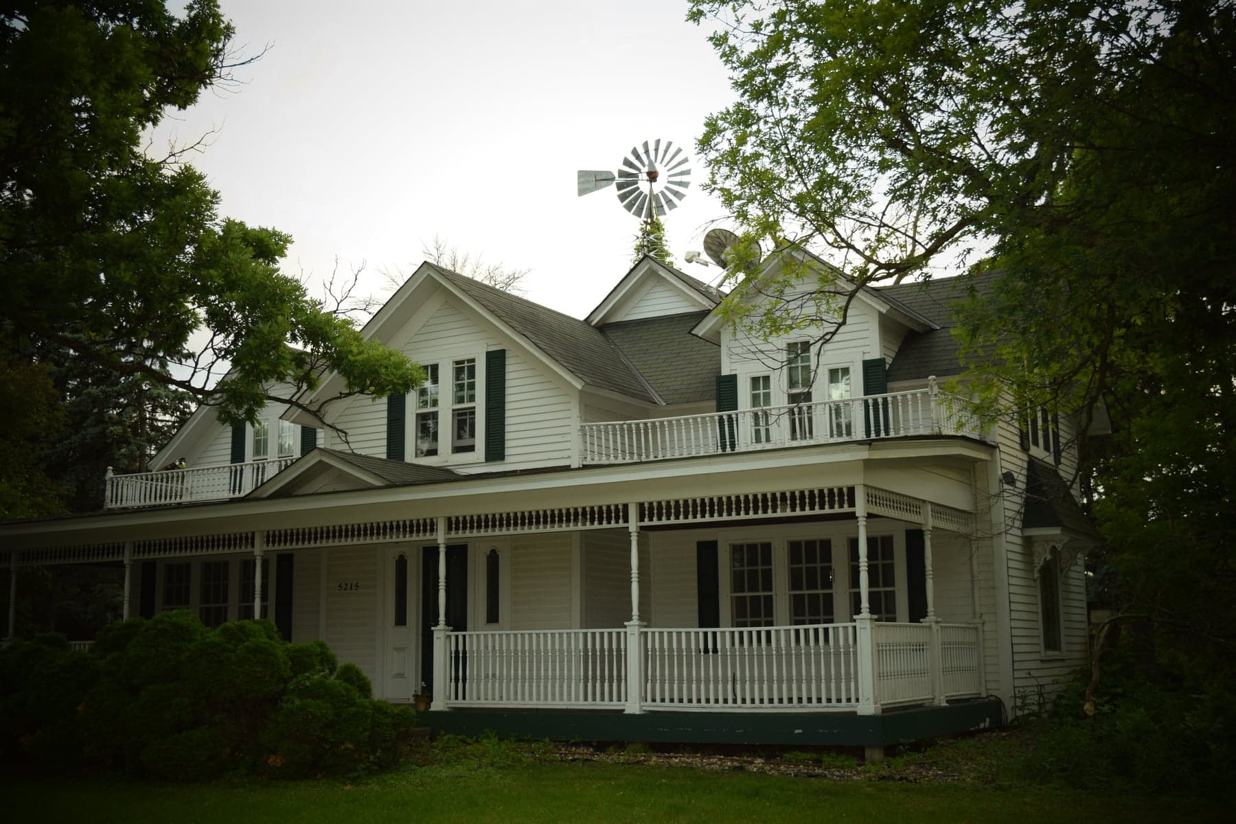 Historic white farmhouse in Plymouth with a wraparound porch and windmill, photographed in June 2026